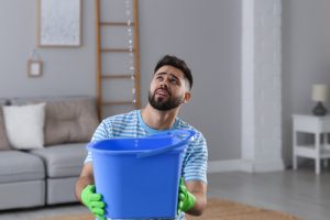 Young,man,collecting,leaking,water,from,ceiling,at,home,,space