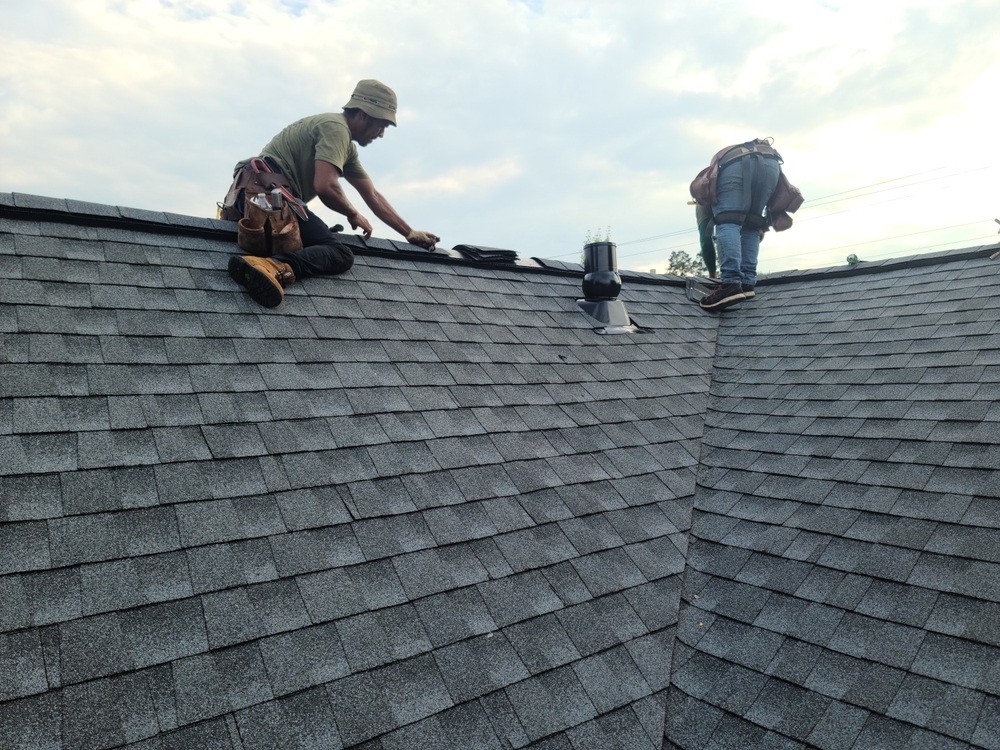 Roofers,installing,shingles,and,ridge,cap,on,the,roof,of